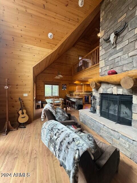 living room featuring wood walls, light wood-type flooring, wood ceiling, a fireplace, and high vaulted ceiling