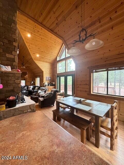 dining area featuring ceiling fan, wood walls, light hardwood / wood-style flooring, high vaulted ceiling, and wooden ceiling