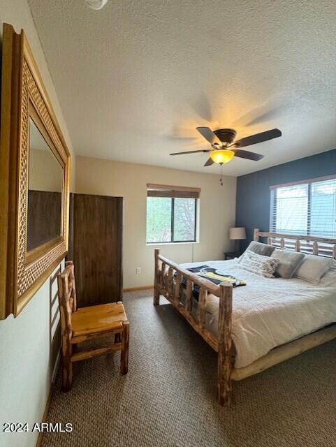 bedroom featuring a textured ceiling, dark colored carpet, multiple windows, and ceiling fan