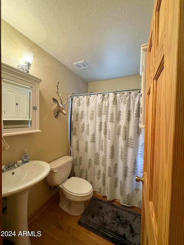 bathroom featuring a shower with shower curtain, hardwood / wood-style flooring, a textured ceiling, and toilet