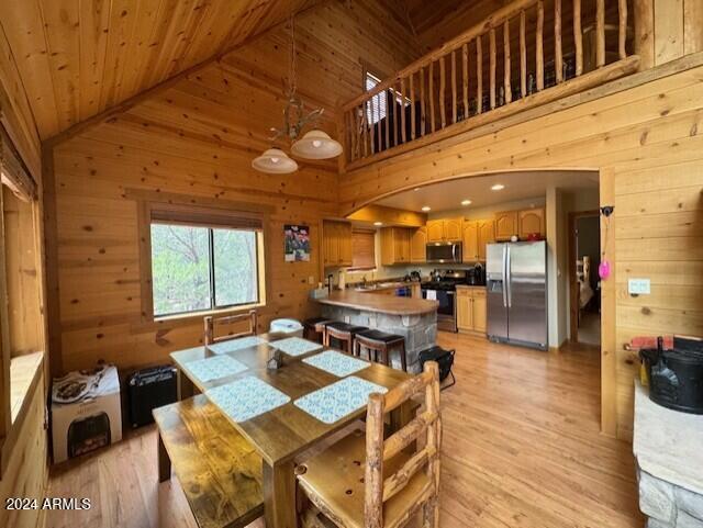 dining room with high vaulted ceiling, wooden walls, wood ceiling, and light hardwood / wood-style flooring