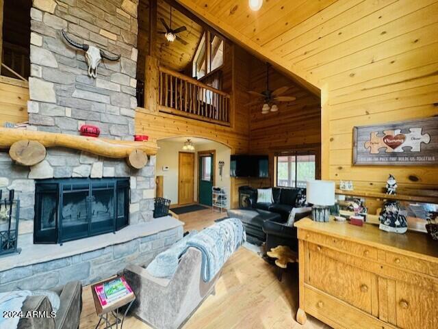 living room featuring wood ceiling, a stone fireplace, wooden walls, high vaulted ceiling, and hardwood / wood-style flooring