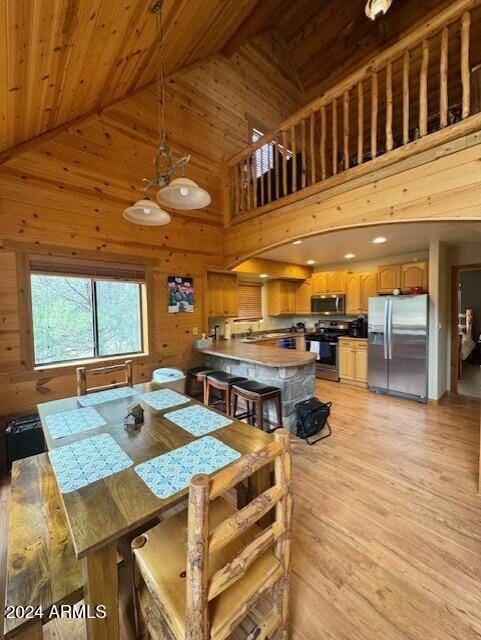 dining room featuring light hardwood / wood-style flooring, wood walls, wood ceiling, and high vaulted ceiling