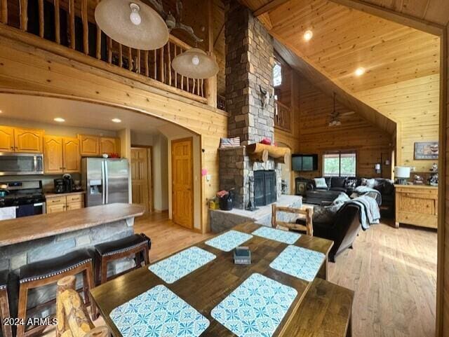 dining space with light wood-type flooring, wood walls, high vaulted ceiling, wooden ceiling, and a fireplace