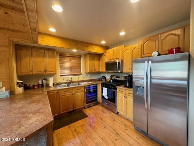 kitchen featuring light wood-type flooring, beverage cooler, beam ceiling, sink, and stainless steel appliances