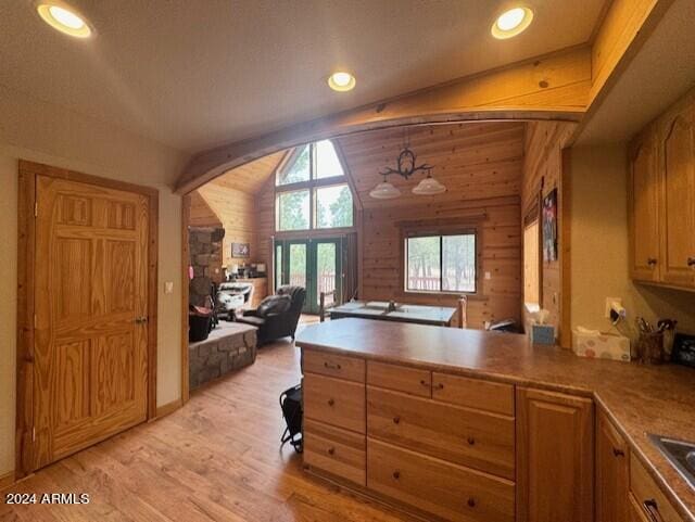 kitchen with wooden walls, decorative light fixtures, lofted ceiling with beams, and light wood-type flooring