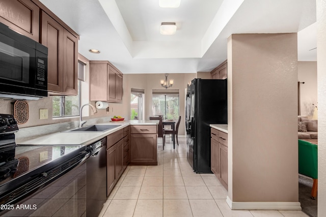 kitchen featuring sink, a raised ceiling, kitchen peninsula, black appliances, and a notable chandelier