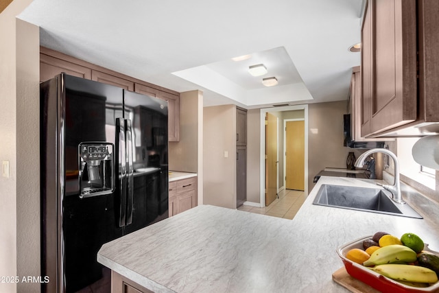 kitchen with kitchen peninsula, light tile patterned floors, black fridge, a tray ceiling, and sink