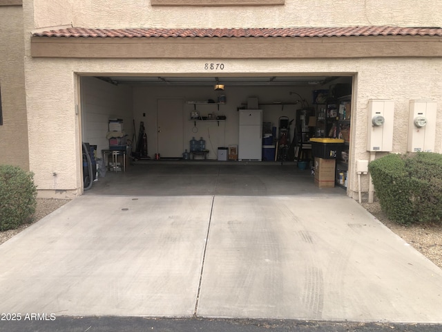 garage featuring freestanding refrigerator and concrete driveway