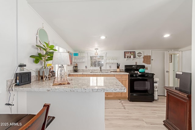 kitchen featuring light hardwood / wood-style floors, kitchen peninsula, sink, black gas range oven, and light brown cabinetry