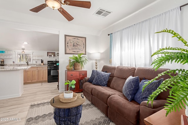 living room featuring ceiling fan, plenty of natural light, sink, and light hardwood / wood-style flooring