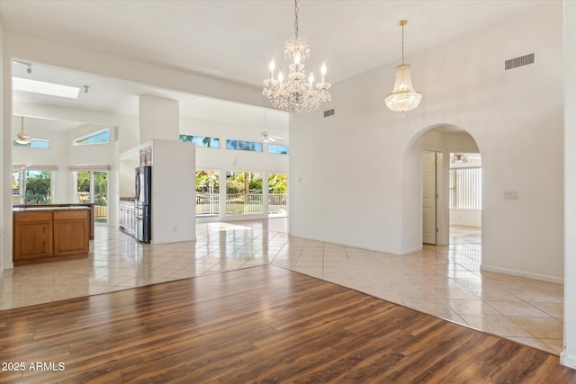 spare room with a high ceiling, ceiling fan with notable chandelier, and light tile patterned floors