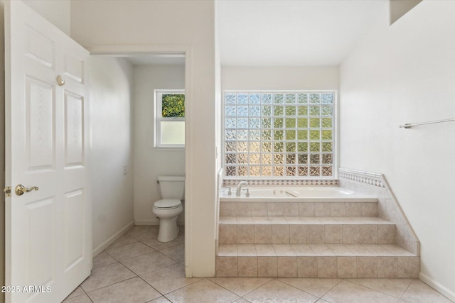 bathroom featuring a relaxing tiled tub, tile patterned flooring, and toilet