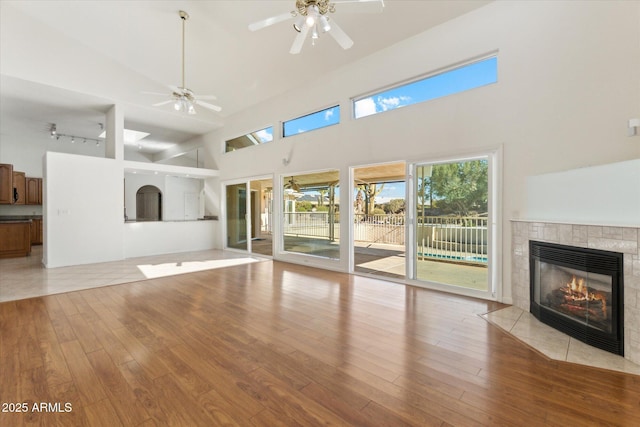 unfurnished living room featuring light wood-type flooring, a tile fireplace, and a towering ceiling