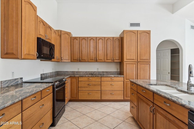 kitchen with sink, light tile patterned flooring, dark stone countertops, and black appliances