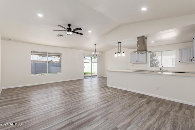 kitchen with island exhaust hood, ceiling fan with notable chandelier, vaulted ceiling, decorative light fixtures, and hardwood / wood-style floors