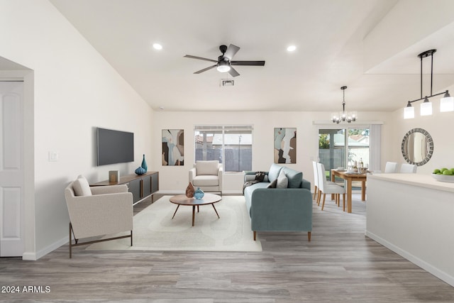 living room with ceiling fan with notable chandelier, lofted ceiling, a wealth of natural light, and light hardwood / wood-style flooring