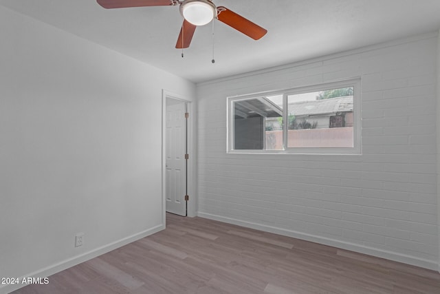 unfurnished room featuring light hardwood / wood-style floors, ceiling fan, and brick wall