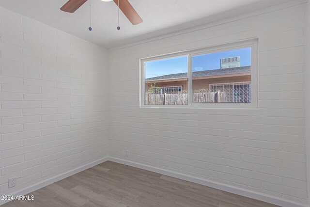 spare room with wood-type flooring, ceiling fan, and brick wall