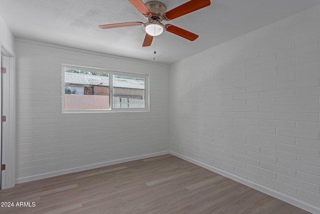 spare room featuring light wood-type flooring, brick wall, and ceiling fan