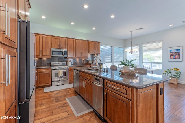 kitchen with appliances with stainless steel finishes, decorative light fixtures, a center island with sink, and light wood-type flooring