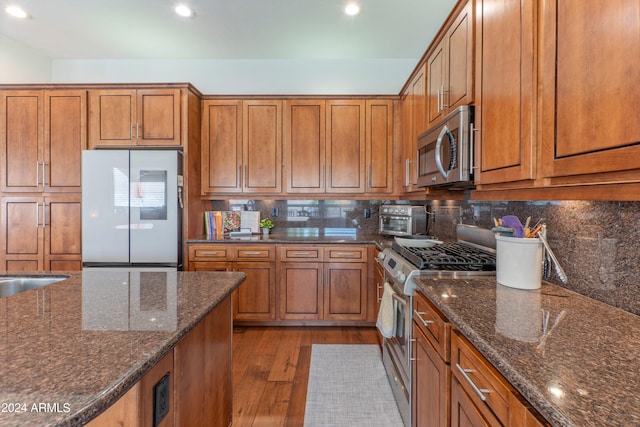 kitchen with light hardwood / wood-style flooring, stainless steel appliances, tasteful backsplash, and dark stone counters