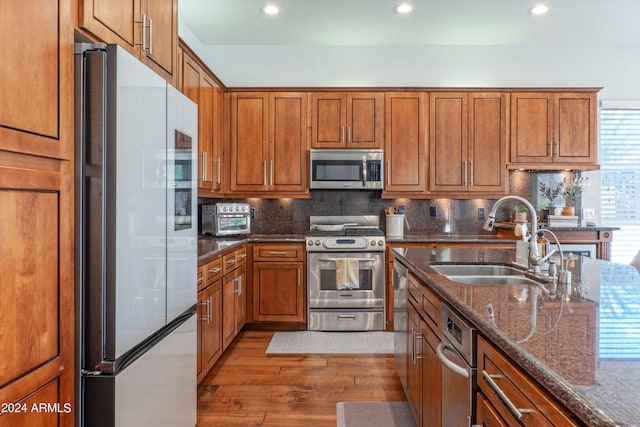 kitchen with tasteful backsplash, appliances with stainless steel finishes, sink, dark stone countertops, and hardwood / wood-style flooring