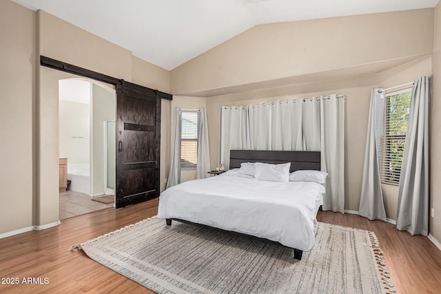 bedroom with vaulted ceiling, a barn door, wood-type flooring, and connected bathroom