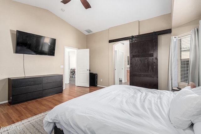 bedroom featuring connected bathroom, lofted ceiling, a barn door, ceiling fan, and wood-type flooring