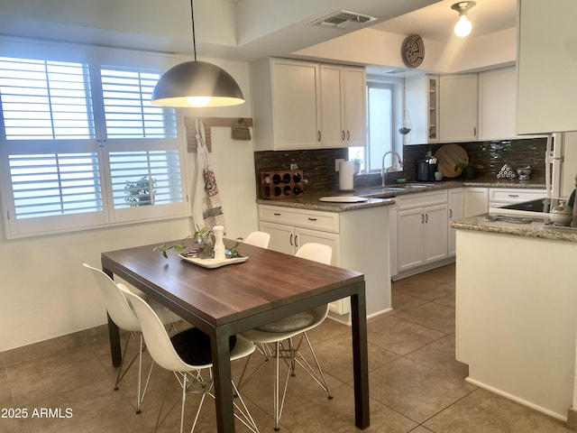 kitchen with hanging light fixtures, white cabinetry, sink, and backsplash