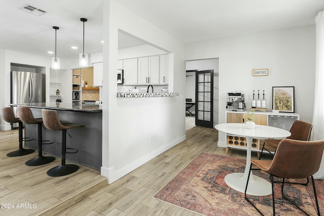 kitchen featuring white cabinets, backsplash, hanging light fixtures, and stainless steel refrigerator