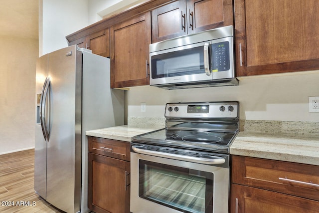 kitchen with light hardwood / wood-style flooring, light stone counters, and stainless steel appliances