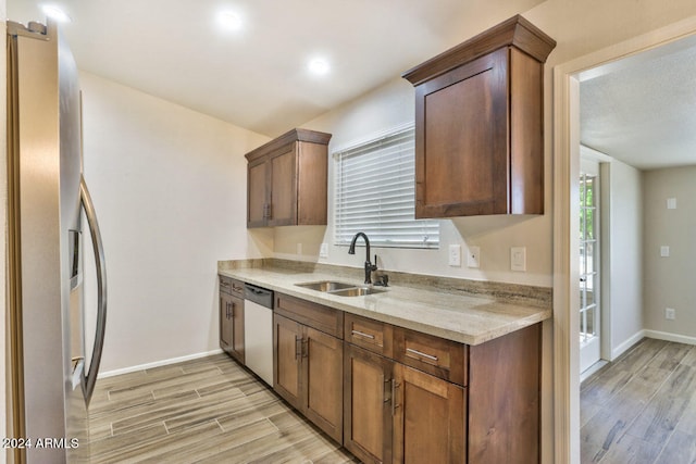 kitchen with sink, appliances with stainless steel finishes, light stone counters, and light hardwood / wood-style floors