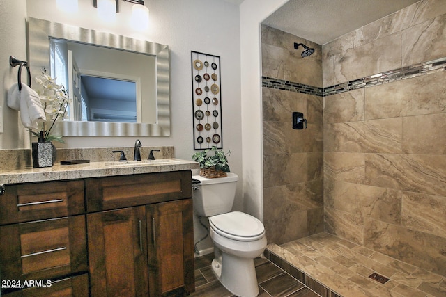 bathroom featuring vanity, a tile shower, a textured ceiling, and toilet