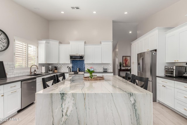 kitchen featuring appliances with stainless steel finishes, a sink, a center island, white cabinets, and a high ceiling
