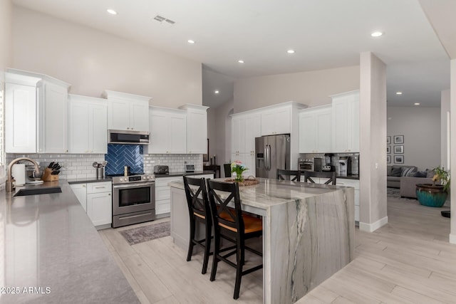 kitchen featuring appliances with stainless steel finishes, a sink, a breakfast bar area, a spacious island, and high vaulted ceiling