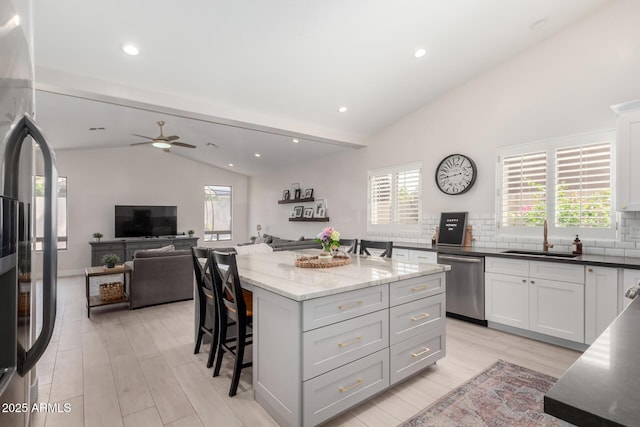 kitchen with stainless steel appliances, a sink, vaulted ceiling, a kitchen bar, and backsplash