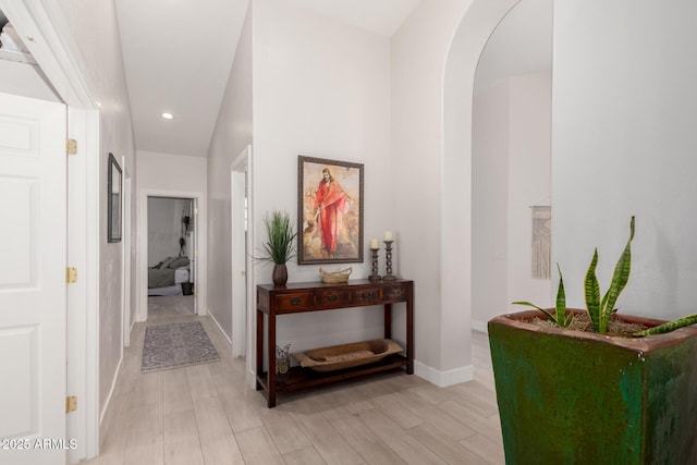 hall featuring light wood-type flooring, arched walkways, baseboards, and recessed lighting