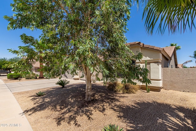view of property hidden behind natural elements with stucco siding, a tile roof, fence, and concrete driveway