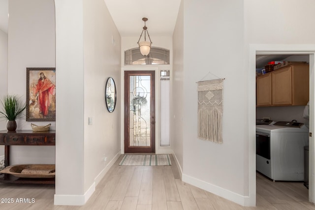 foyer entrance with light wood-style flooring, independent washer and dryer, baseboards, and a high ceiling