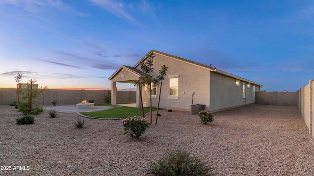 property exterior at dusk with a patio, stucco siding, an outdoor fire pit, central AC, and a fenced backyard