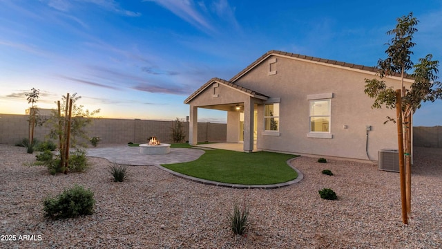 back of property at dusk with stucco siding, an outdoor fire pit, a patio area, cooling unit, and a fenced backyard