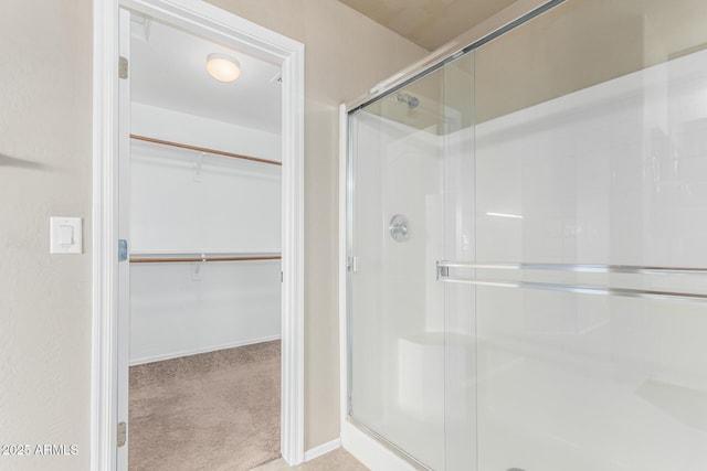 bathroom with baseboards, a walk in closet, and a stall shower