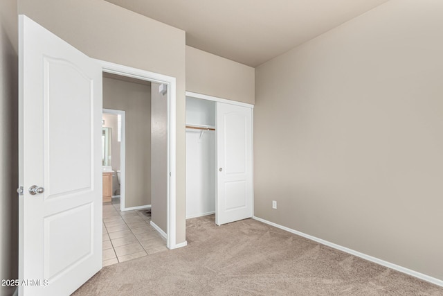 unfurnished bedroom with baseboards, light colored carpet, light tile patterned floors, and a closet