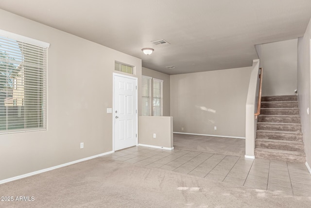 carpeted empty room with tile patterned floors, visible vents, baseboards, and stairway