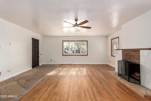 unfurnished living room with light hardwood / wood-style floors, a stone fireplace, and ceiling fan