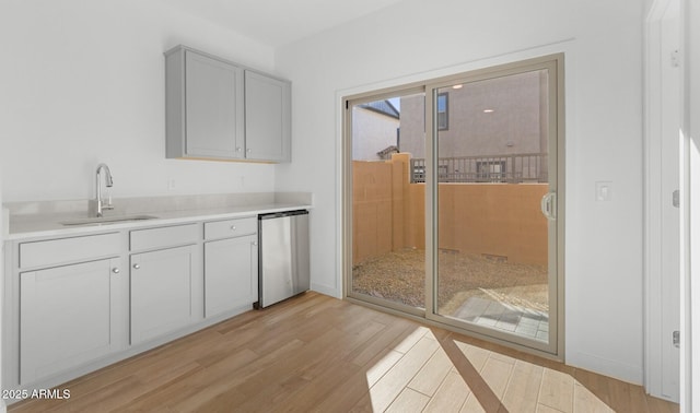 kitchen featuring light wood finished floors, baseboards, light countertops, refrigerator, and a sink