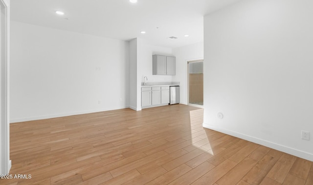 unfurnished room featuring recessed lighting, light wood-style flooring, baseboards, and a sink