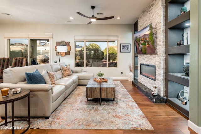 living room featuring dark hardwood / wood-style flooring, ceiling fan, a fireplace, and built in shelves