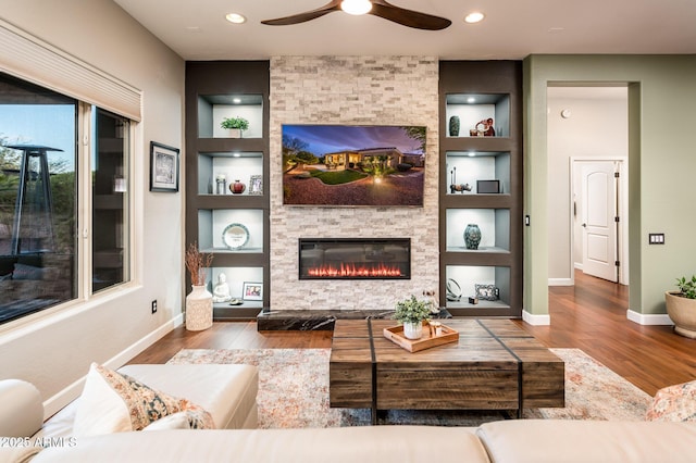 living room with built in shelves, wood-type flooring, and a stone fireplace